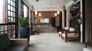 A spacious lobby with a stone wall, wooden furniture, and large windows. - Delta Maresias Club by SmartSharing (São Sebastião)
