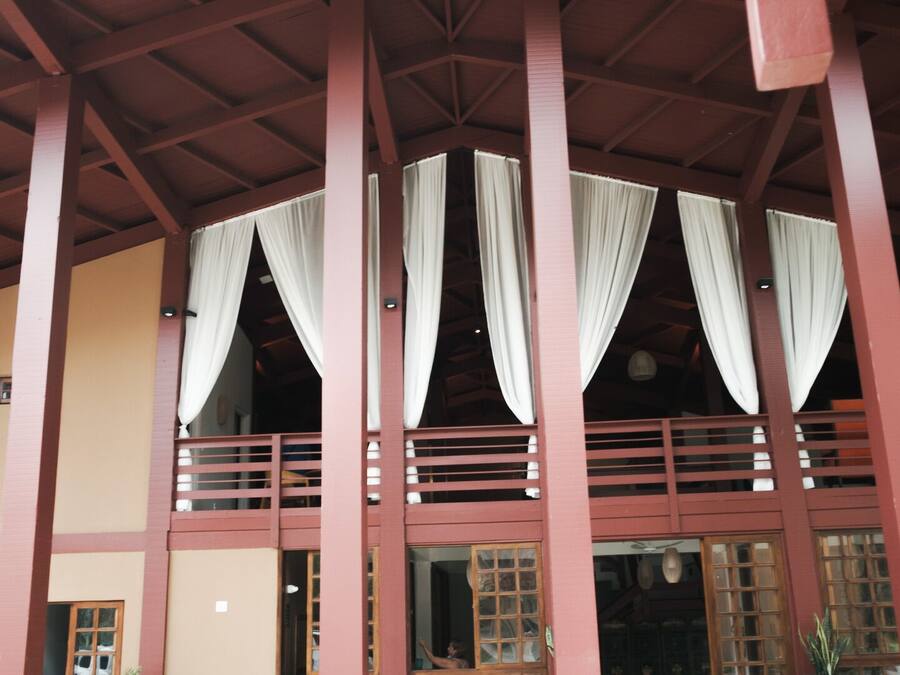 A building with a red wooden structure, multiple windows with white curtains, and a balcony with a railing.