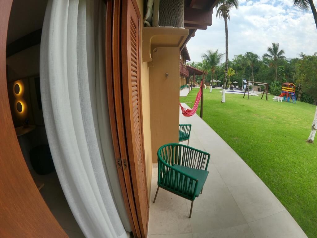 Vista de una habitación de hotel con un ventanal grande, una silla verde y una hamaca en el exterior.