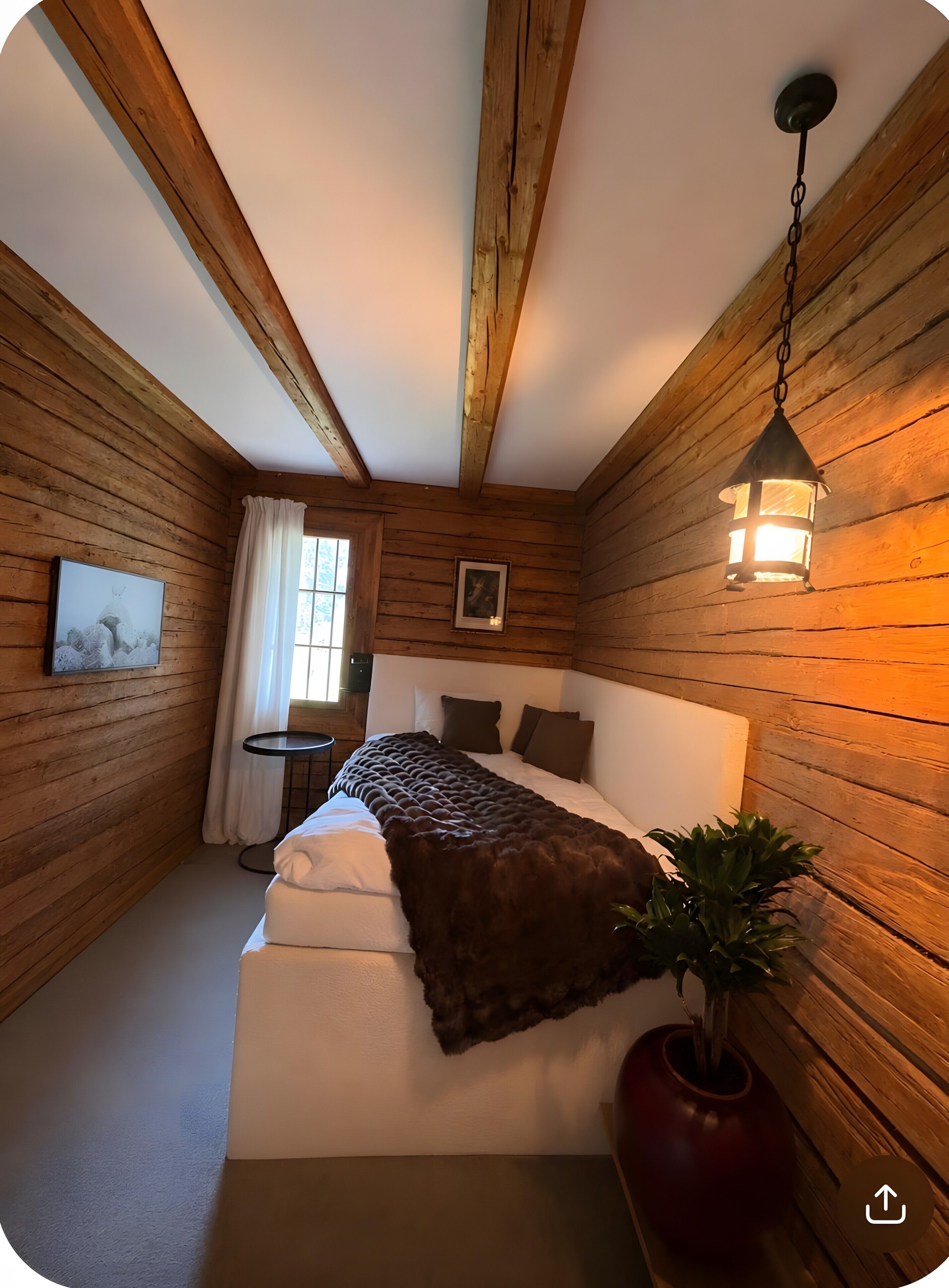 Ein Zimmer mit Holzwänden, einem Bett, einem kleinen Tisch und einem Blumentopf.