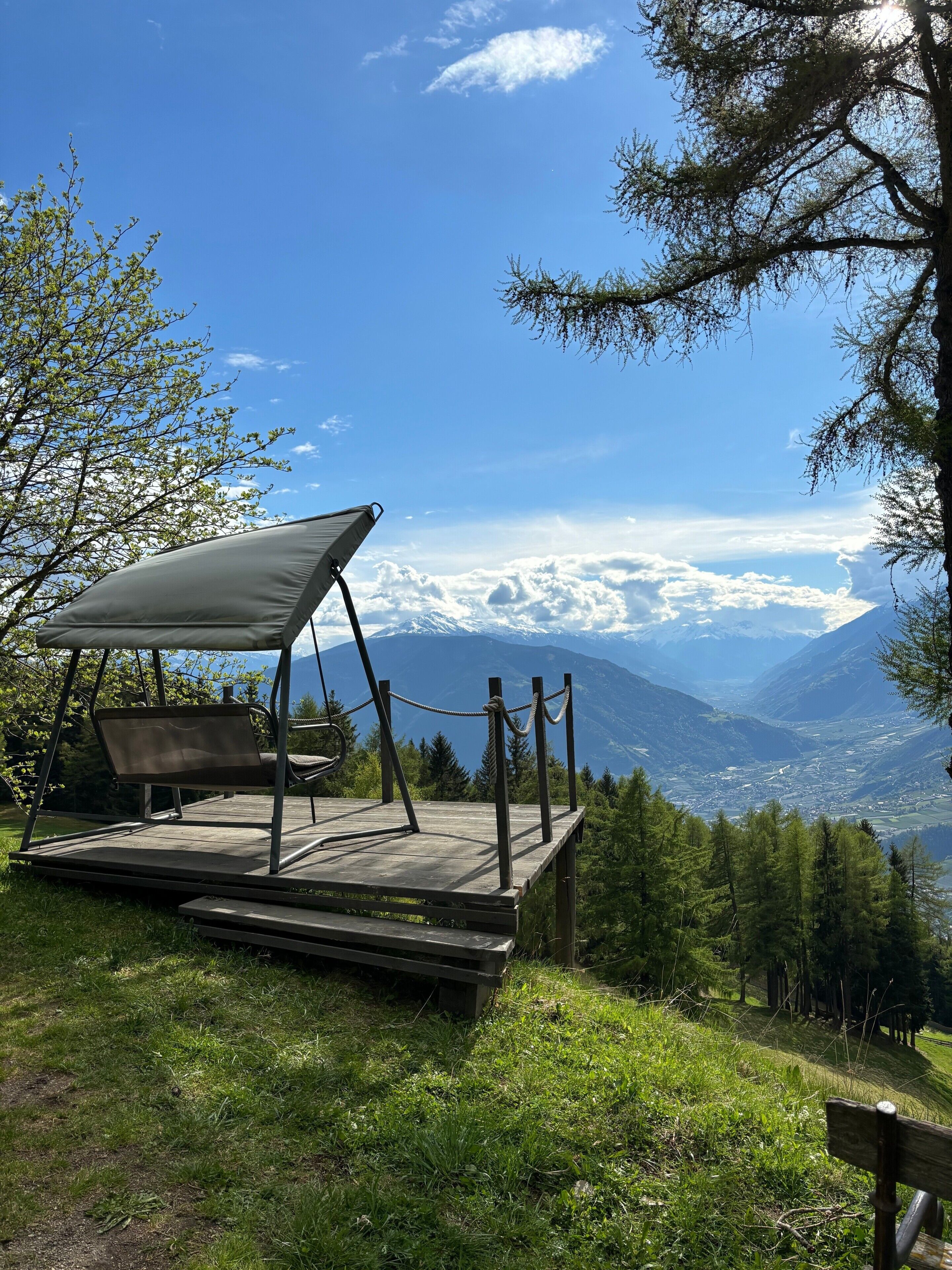 Ein Campingplatz mit einer Schaukelstuhlsitzgelegenheit und einem Picknicktisch, umgeben von Bäumen und einer gebirgigen Landschaft.