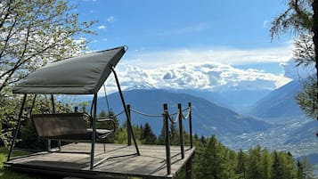 Ein Campingplatz mit einer Schaukelstuhlsitzgelegenheit und einem Picknicktisch, umgeben von Bäumen und einer gebirgigen Landschaft.