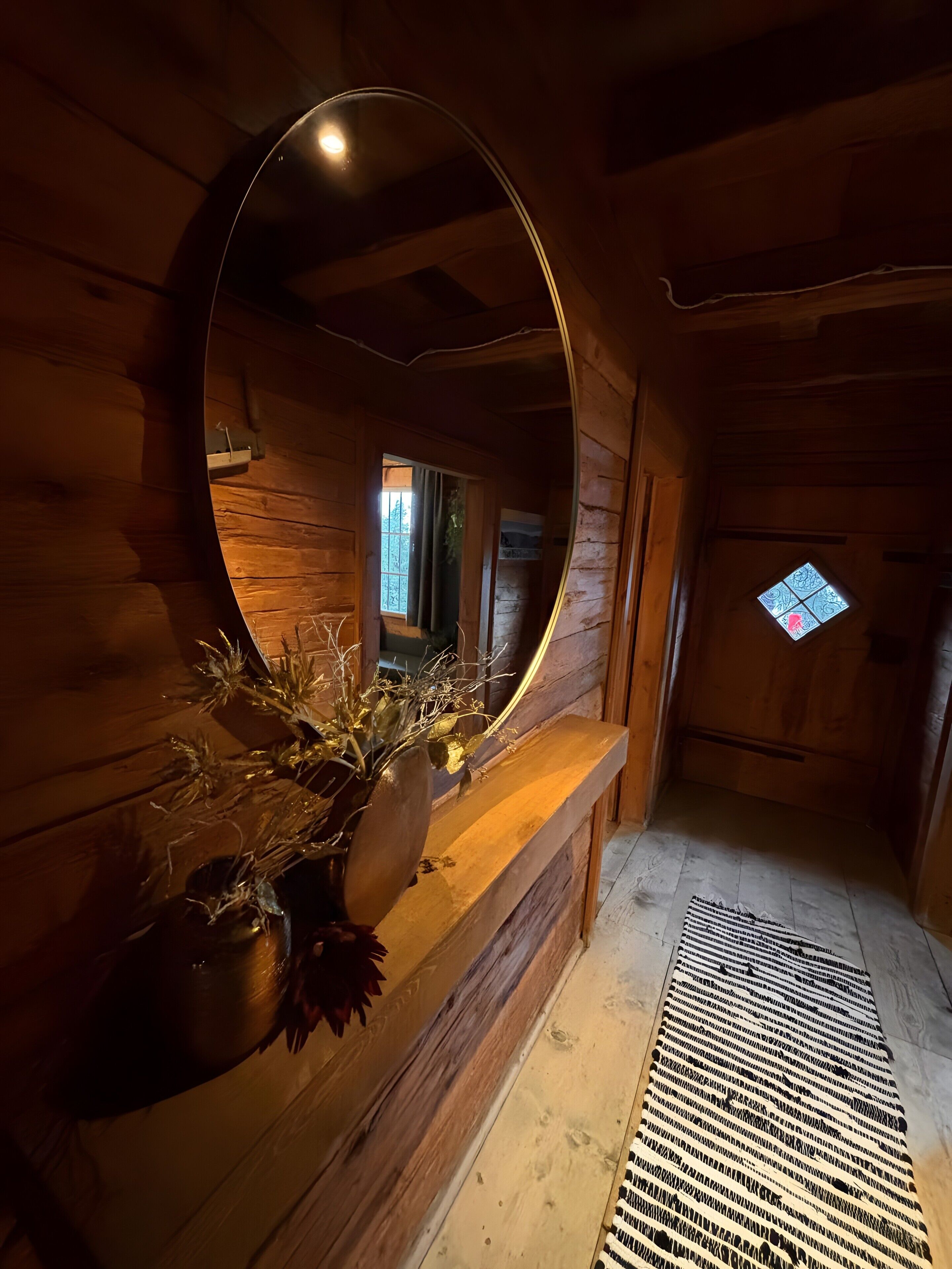 A wooden interior with a round mirror, a wooden bench, and a small window.