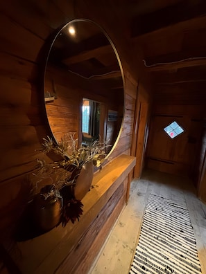 A wooden interior with a round mirror, a wooden bench, and a small window.