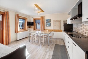 Une cuisine moderne avec des meubles blancs, un plan de travail noir et une table à manger en bois, accompagnée de chaises.