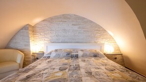 A bedroom with a stone wall arch, a bed with a patterned bedspread, two bedside lamps, and a sofa. - Holiday Home "Sg Standard" with Landmark View, Terrace & Wi-Fi (Massafra)