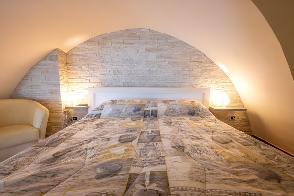 Un dormitorio con arco de pared de piedra, una cama con colcha estampada, dos lámparas de noche y un sofá.