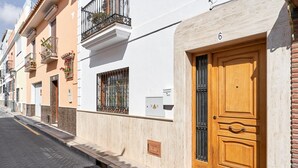 A row of buildings with a prominent wooden door, a balcony with flowers, and a number '6' on the wall. - Holiday Home Casa Murillo with Sea View, Terrace & Wi-Fi (Nerja)