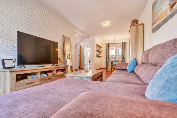 Un salon moderne doté d’un téléviseur à écran plat, d’un grand canapé, d’un meuble de rangement en bois et d’un mur en briques.