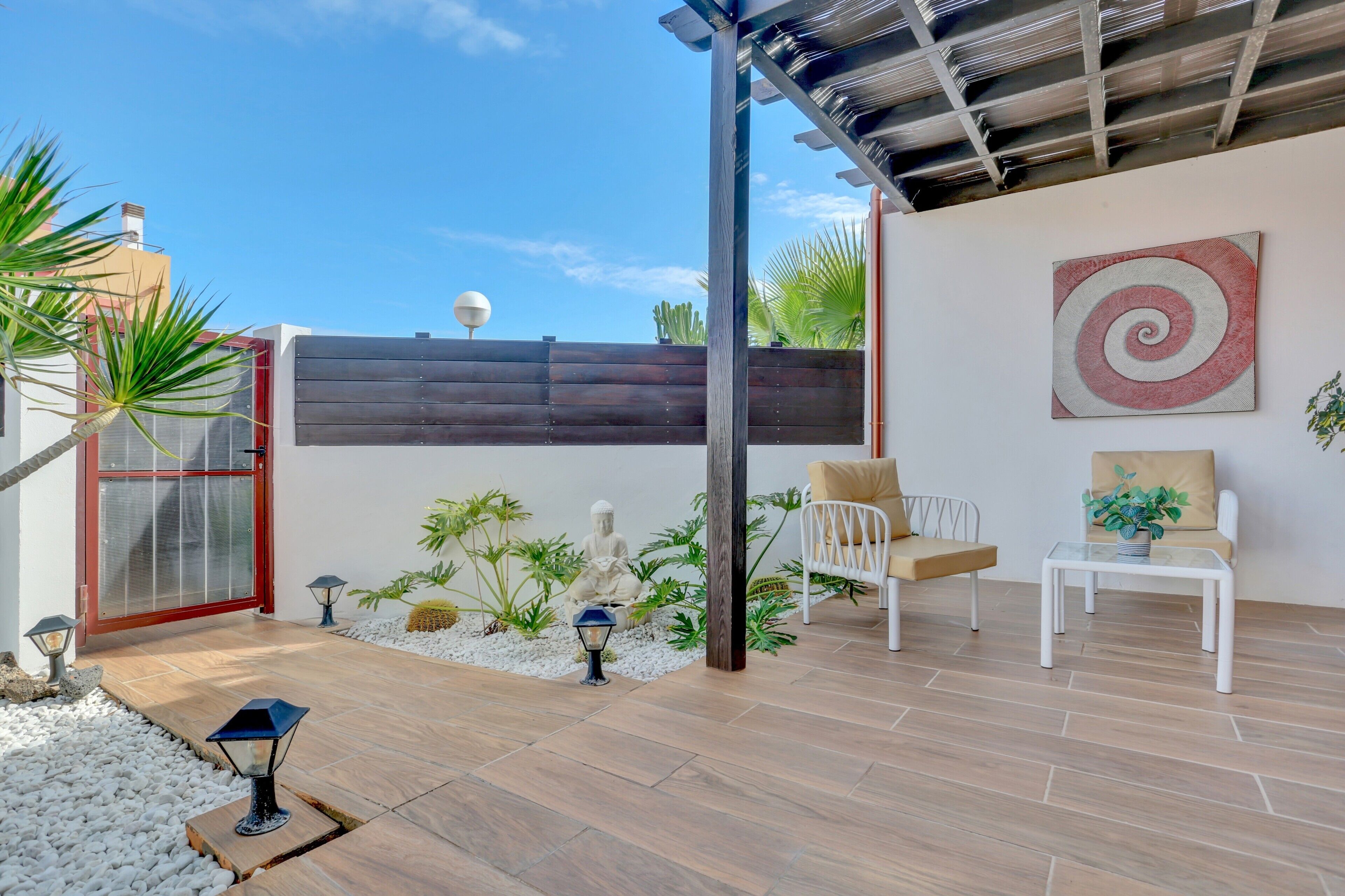 Un patio moderno con zona de estar, una obra de arte espiral decorativa y diversas plantas.