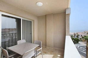 A balcony with a table and chairs, a view of the sea, and a building in the background.