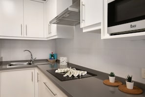 A modern kitchen with white cabinets, a stainless steel sink, a microwave, and two potted plants on round coasters.
