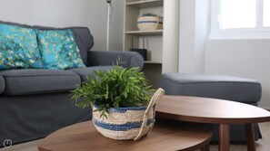 En stue med en grå sofa, en blå og hvid vævet kurv med en plante, og et træbord.