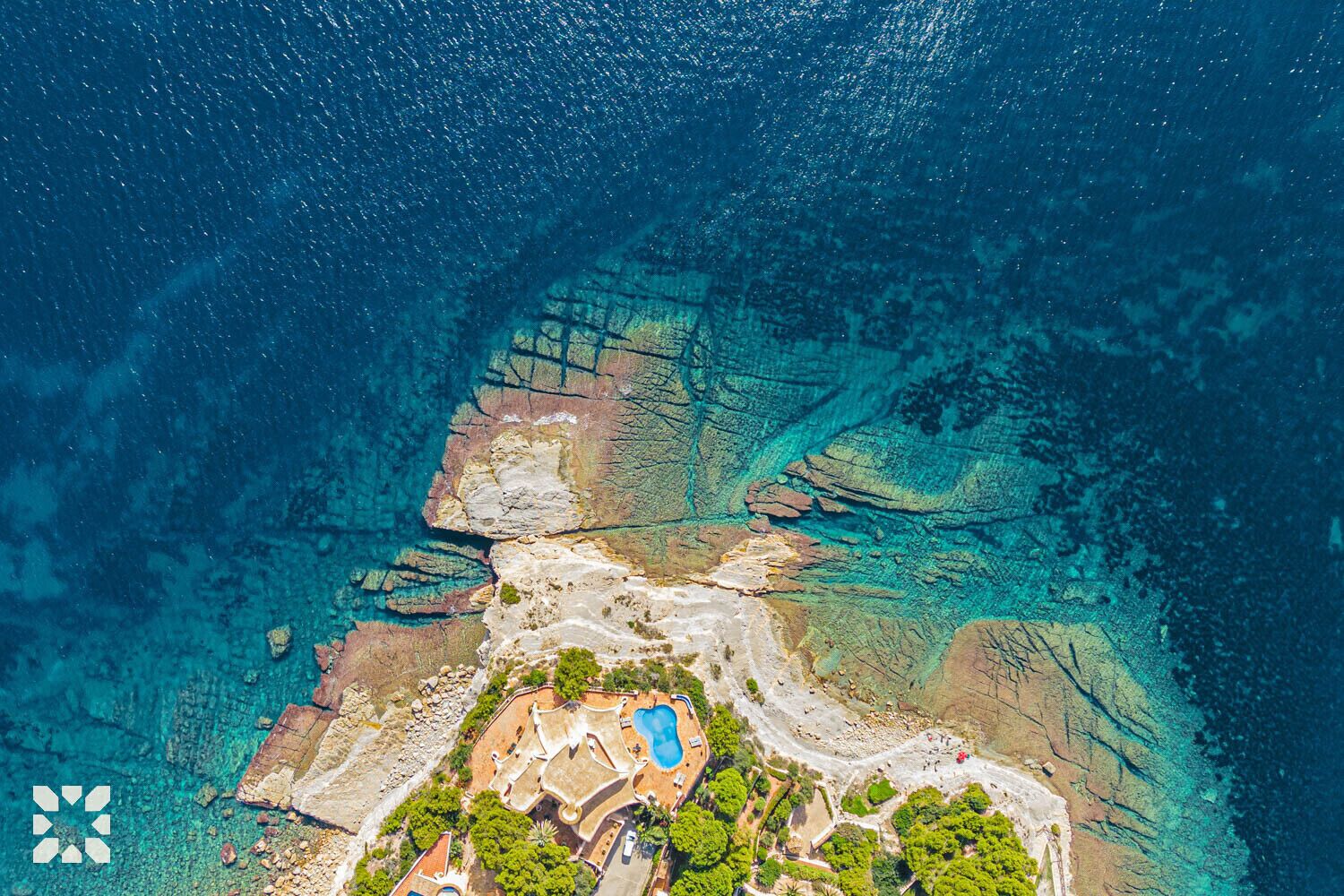Ein Luftbild eines Küstengrundstücks mit Schwimmbad, felsigem Gelände und klarem, blauem Wasser.