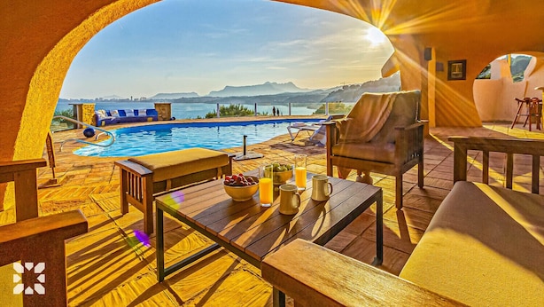 A poolside area with a view of the sea, outdoor seating, and a table with fruits and drinks. - Villa DIANA by Abahana Villas (Teulada)