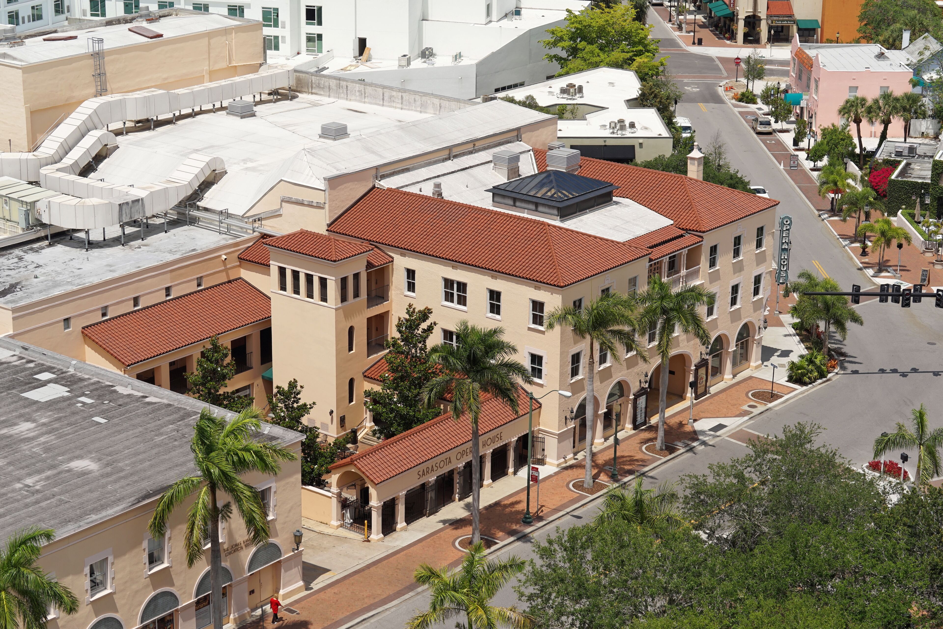A multi-story building with a red-tiled roof, arched windows, and a central courtyard with palm trees.