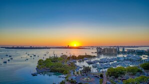 Uma marina com vários barcos, uma ponte e edifícios ao fundo durante o pôr do sol.