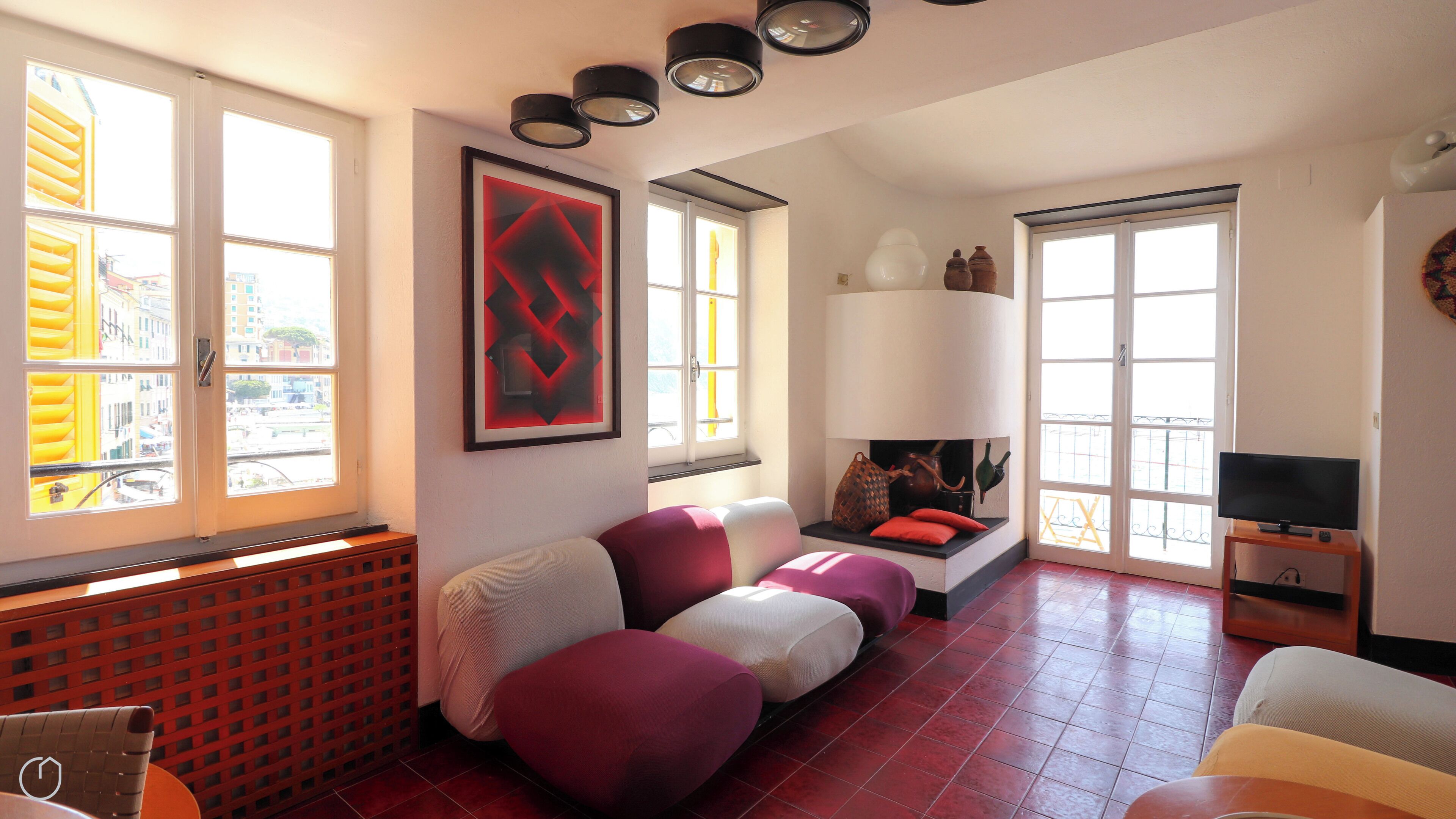 Una sala de estar moderna con chimenea, sofás rojos y blancos, un televisor y ventanas amplias con vistas a la ciudad.