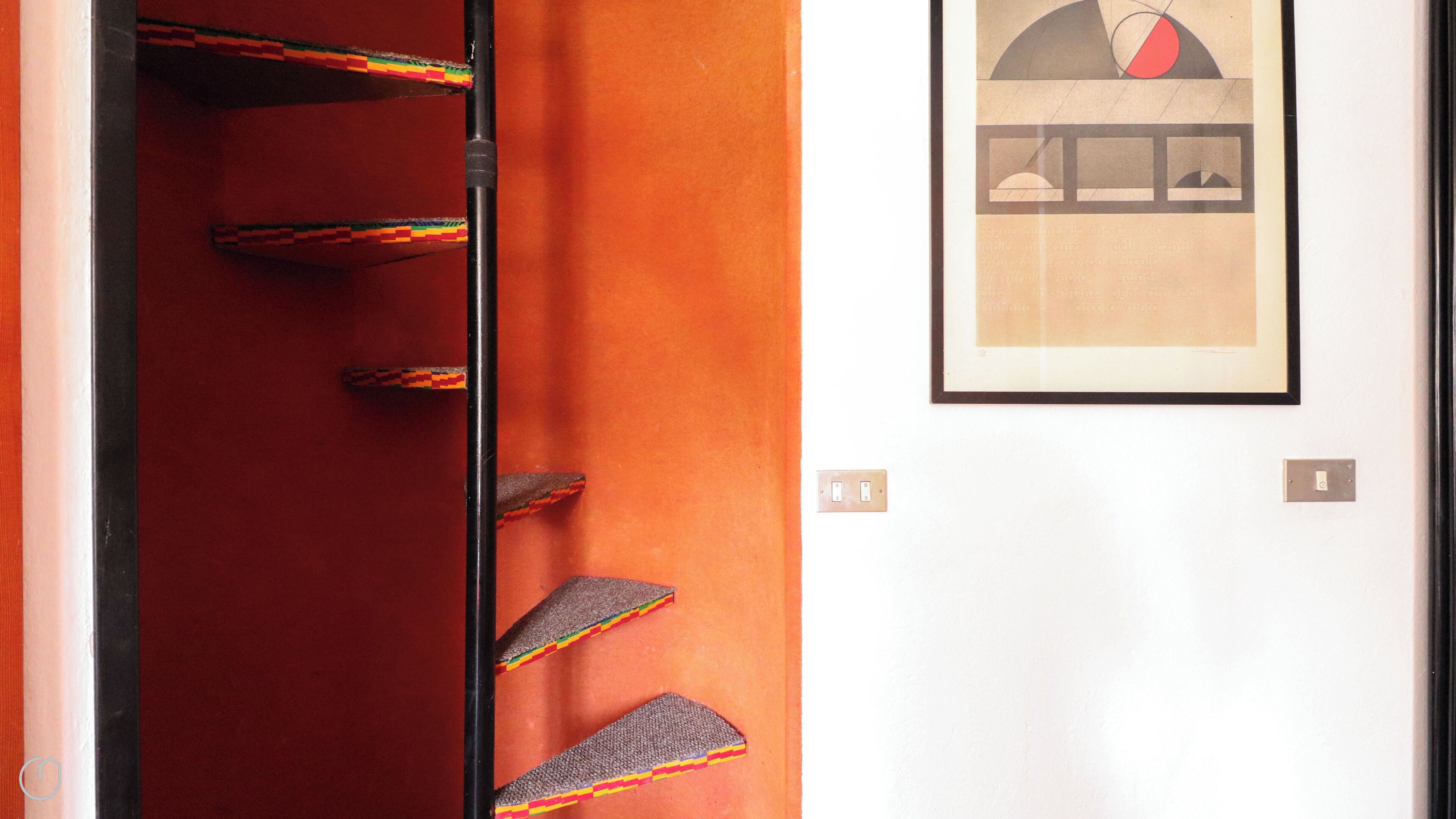 A hotel lobby with a red carpet, a framed artwork on the wall, and a staircase with colorful steps.