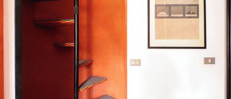 A hotel lobby with a red carpet, a framed artwork on the wall, and a staircase with colorful steps.