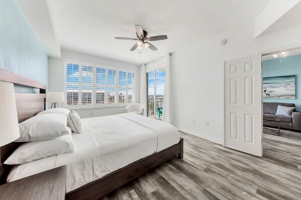 Un dormitorio con cama, ventilador de techo, vista a la ciudad y una puerta que da a otra habitación.