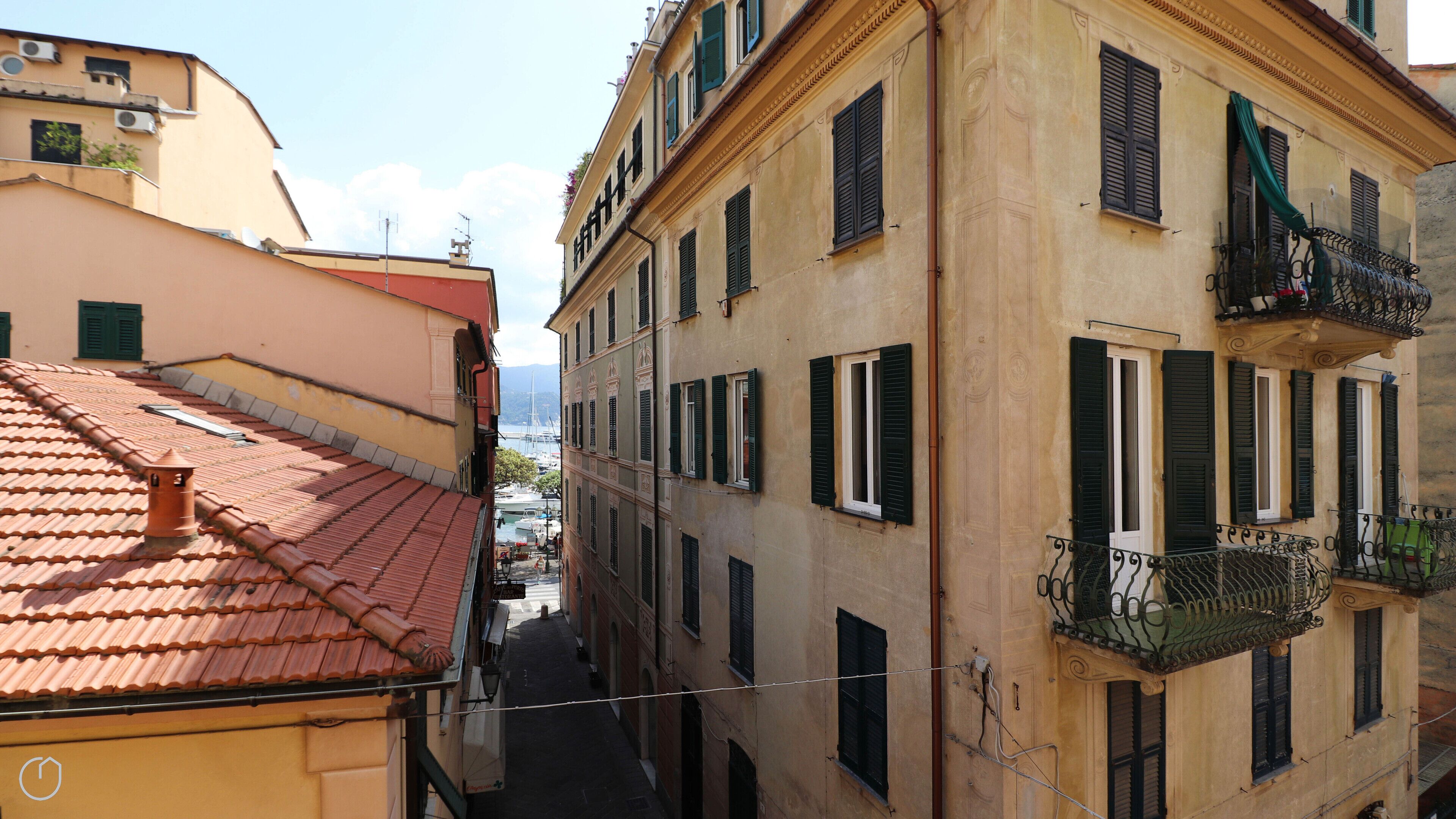 A narrow street with buildings featuring traditional architecture, including balconies with wrought iron railings and shutters.