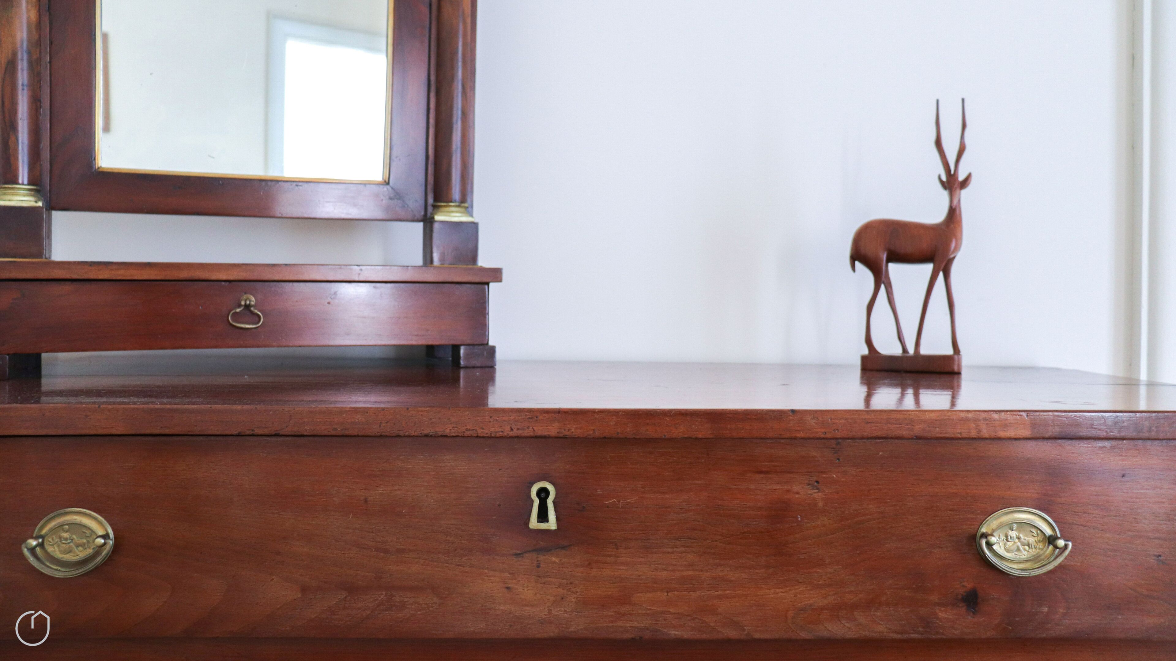 Une commode en bois, surmontée d’un miroir et d’une figurine de cerf.
