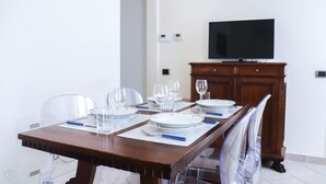 A dining area with a wooden table set for four, clear chairs, and a television on the wall. - Italianway - Ruffini 20 (Santa Margherita Ligure)