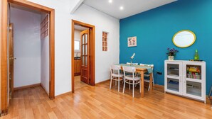 A room with a wooden floor, a blue accent wall, a dining table with chairs, a white cabinet with books, and a wooden door. - Tranquilo. Cerca de la Playa. Bien Comunicado (Sant Adrià de Besòs)