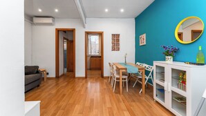 A modern living room with a wooden floor, a sofa, a dining table with chairs, a white cabinet with shelves, and a blue accent wall. - Tranquilo. Cerca de la Playa. Bien Comunicado (Sant Adrià de Besòs)