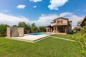 A two-story house with a swimming pool, a patio, and a well-maintained lawn.