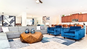 Un salon moderne avec un canapé d’angle gris, des fauteuils en velours bleu et une table basse en bois.