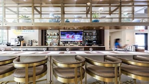 Un espace bar doté d’un long comptoir, de nombreux tabourets et d’un écran de télévision diffusant un événement sportif.