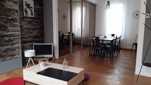 Uma sala de estar moderna com televisão, área de jantar com cadeiras e uma janela grande.