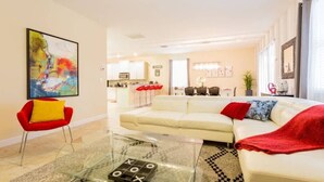 A modern living room with a glass coffee table, a red chair, a white sofa, and a colorful abstract painting on the wall.