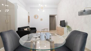 A modern living room with a glass dining table, black sofa, and a TV on a wooden cabinet. - Gioberti 11 (Sesto San Giovanni)
