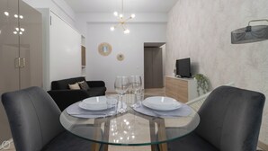 A modern living room with a glass dining table set for two, a black sofa, and a TV on a wooden cabinet. - Gioberti 11 (Sesto San Giovanni)