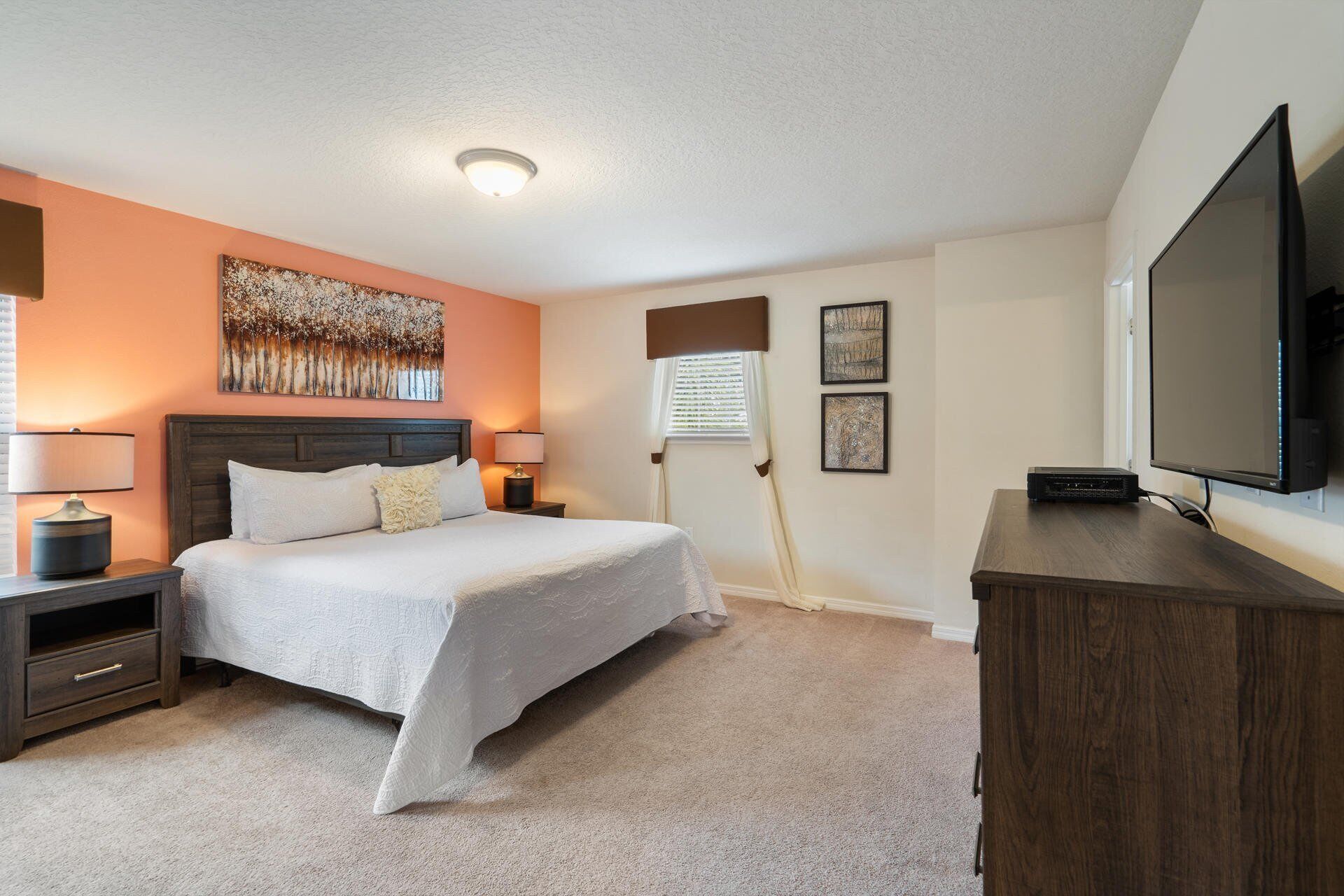 A bedroom with a bed, bedside tables, a TV, and artwork on the walls.