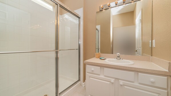 A bathroom with a glass shower enclosure, a sink, and a mirror with lights above it.