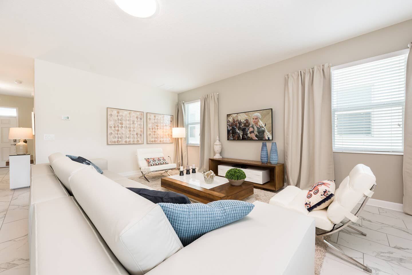 A modern living room with a white sofa, a coffee table, and a TV. There are decorative items on the coffee table and artwork on the walls.