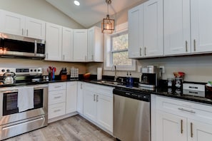 A modern kitchen with white cabinets, stainless steel appliances, and a window providing natural light.