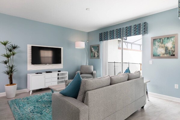 Una sala moderna con un sofá gris, un mueble de entretenimiento blanco, un televisor de pantalla plana grande y una planta en maceta.
