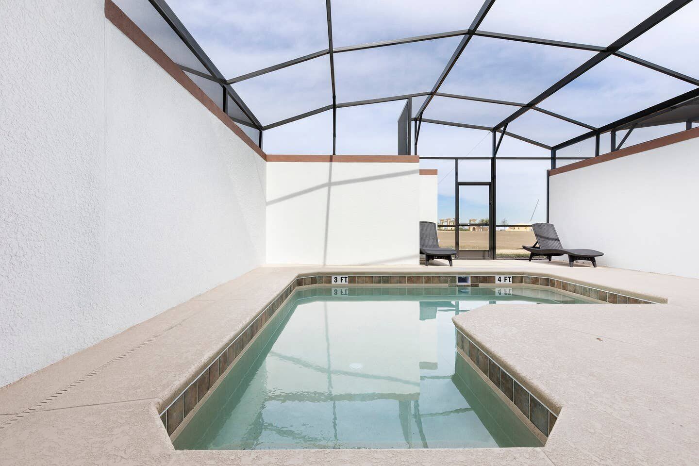 A swimming pool with a glass enclosure, two lounge chairs, and a clear sky view.