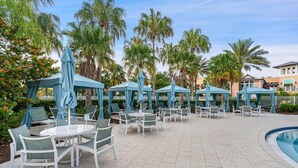 A poolside area with outdoor seating and umbrellas, surrounded by palm trees. - Last Minute Disney Getaway! Villa with Private Pool & Hot Tub. Book Now! #22026 (Orlando)