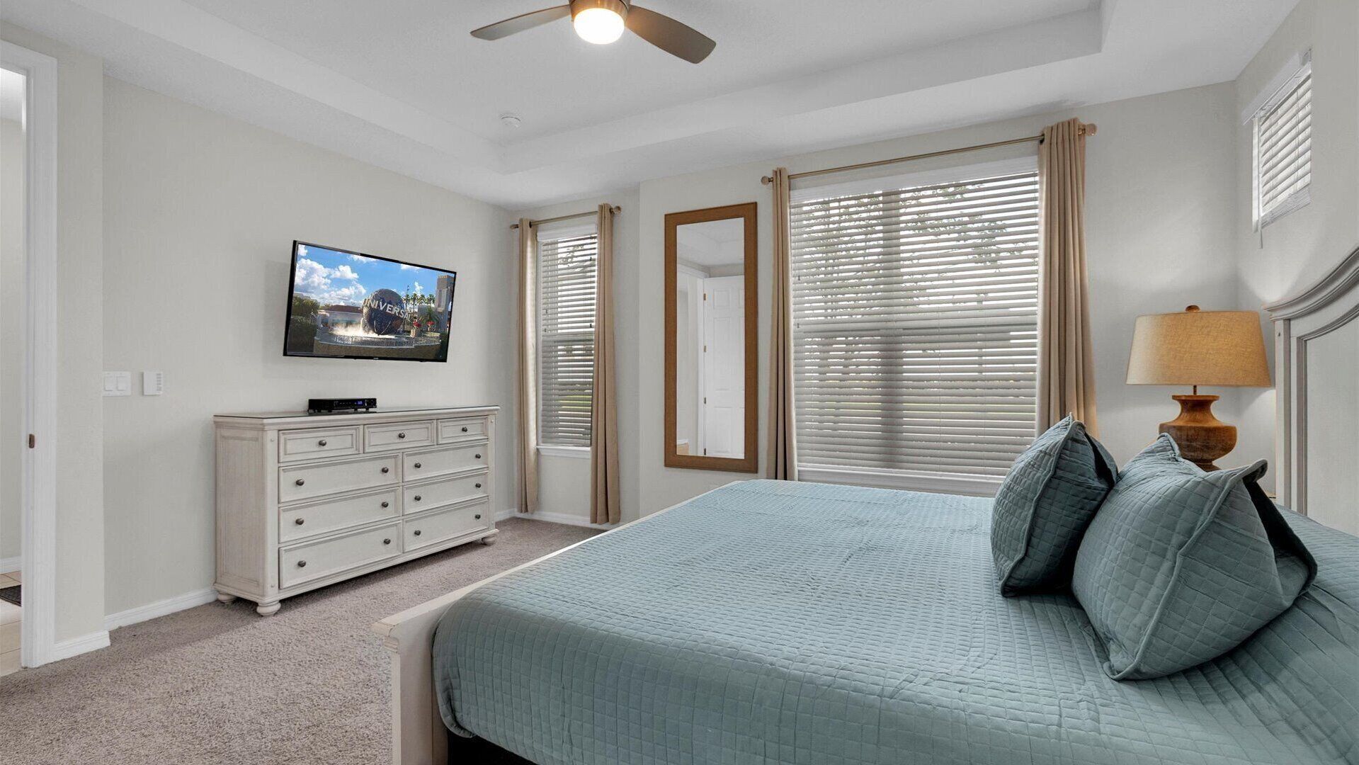 Een slaapkamer met een bed, een dressoir, een televisie en een plafondventilator.