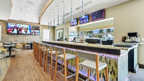 A modern bar area with a long counter, bar stools, and a television screen displaying sports. - Last Minute Disney! Private Pool, Hot Tub, Game Room & Themed Bedrooms. Book Now! #31744 (Orlando)
