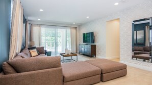 A modern living room with a sectional sofa, a TV on the wall, and a large window with curtains. - Last Minute Disney! Private Pool, Hot Tub, Game Room & Themed Bedrooms. Book Now! #31744 (Orlando)