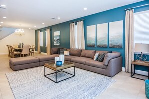 Uma sala de estar moderna com um sofá seccional, uma mesa de centro de vidro e um espaço de jantar com mesa e cadeiras.