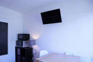 A room with a white wall, a flat-screen TV mounted above a table, a microwave, and a lamp.