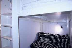 A bunk bed with a patterned pillow, a shelf unit, and a wall-mounted light fixture.